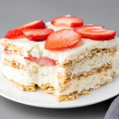 A slice of No Bake Strawberry Cheesecake Icebox Cake showing creamy layers, fresh strawberries, and soft graham crackers.