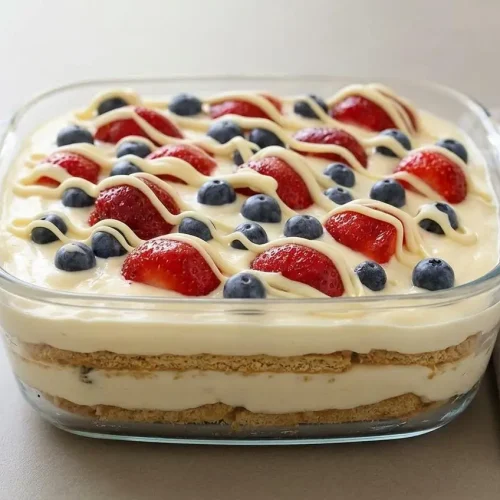 Sliced no-bake summer berry icebox cake with layers of graham crackers, vanilla cream, fresh strawberries, and blueberries.