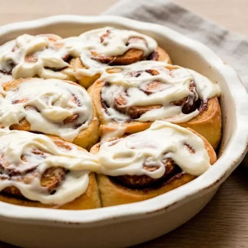 A rectangular baking dish filled with soft overnight cinnamon rolls, generously topped with melted cream cheese icing.