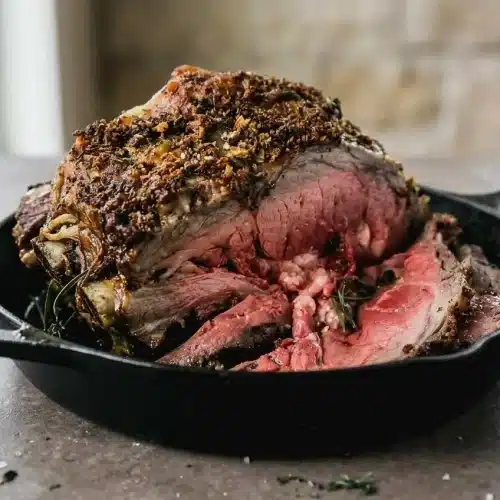 A perfectly cooked prime rib roast recipe with a dark herb and garlic crust, sliced to show a juicy, rosy pink interior.