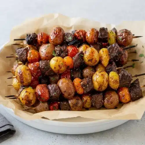 Four rosemary garlic steak kebabs with a glossy balsamic glaze, arranged on a white platter with fresh rosemary.