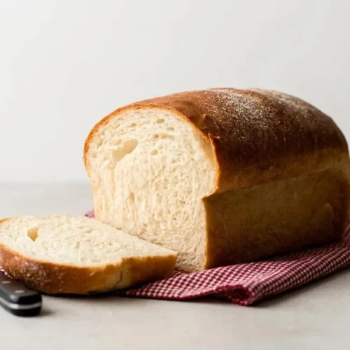 A partially sliced loaf from a sandwich bread recipe, showing a soft crumb and golden brown crust on a wire rack.