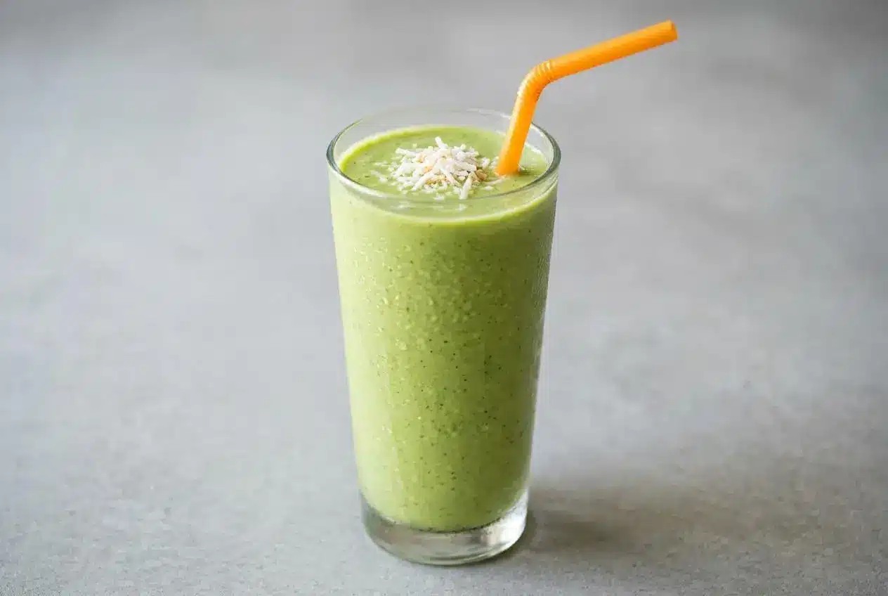 A finished Skinny Green Tropical Smoothie in a tall glass, showing a creamy pale green texture, surrounded by fresh pineapple, spinach, and