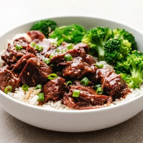 A dark ceramic bowl filled with Slow Cooker Korean Beef, showing tender beef cubes coated in a glossy, sweet and spicy gochujang sauce.