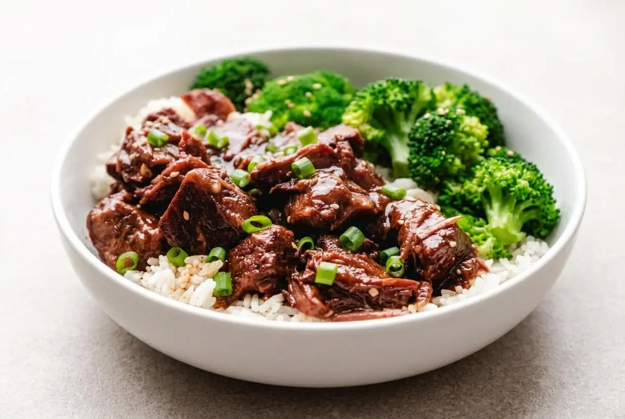 A dark ceramic bowl filled with Slow Cooker Korean Beef, showing tender beef cubes coated in a glossy, sweet and spicy gochujang sauce.