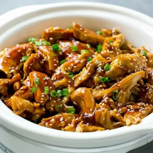 Slow Cooker Teriyaki Chicken in a white bowl, showing tender shredded chicken coated in a glossy homemade sauce and garnished with sesame
