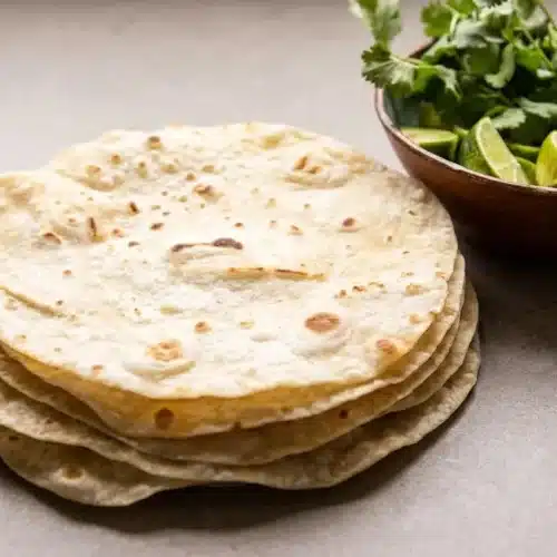 A stack of soft, pliable homemade flour tortillas on a white ceramic plate, ready to be served.