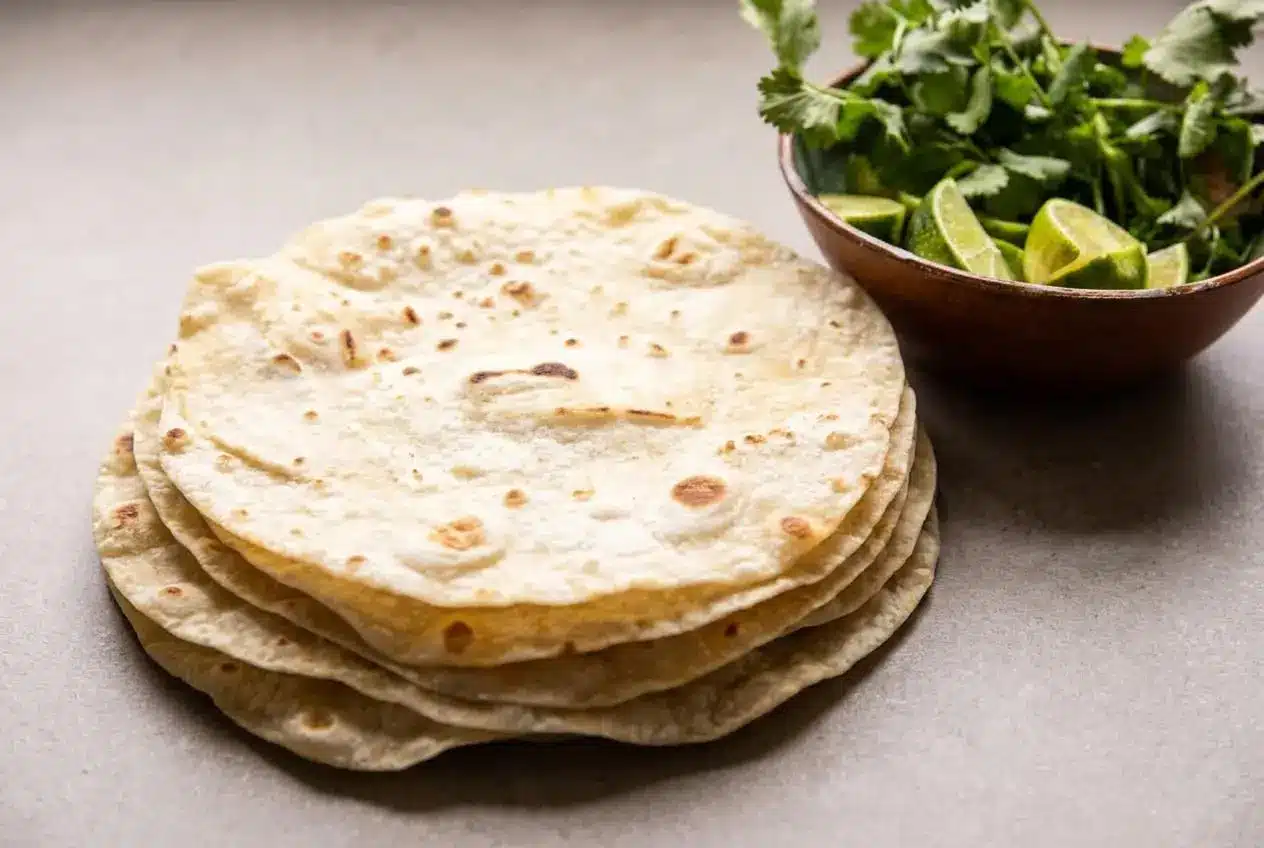 A stack of soft, pliable homemade flour tortillas on a white ceramic plate, ready to be served.