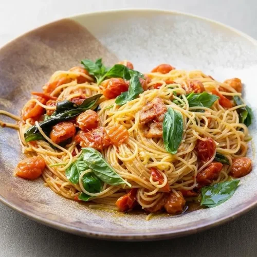 A white bowl of Tomato Basil Pasta with a glossy cherry tomato sauce, fresh basil, and grated pecorino cheese, seen from above.