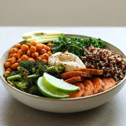 A vegan quinoa bowl filled with fluffy quinoa, roasted broccoli, sriracha chickpeas, and curry sweet potatoes in a white ceramic bowl.