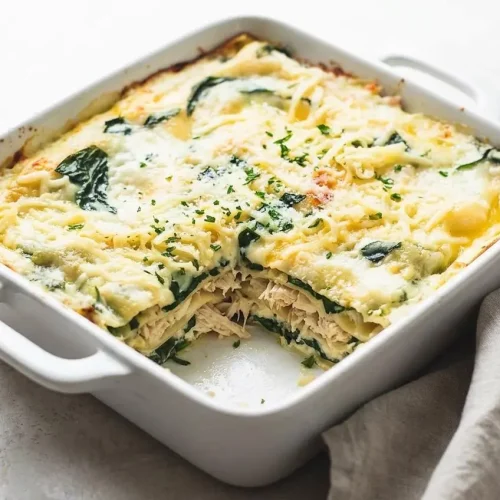 A single slice of White Chicken Lasagna on a white plate, showing creamy layers of chicken and spinach with a golden brown cheesy top.