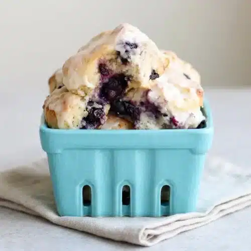 Warm blueberry biscuits drizzled with vanilla glaze showing tall flaky layers and juicy berries.