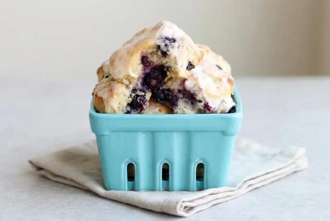Warm blueberry biscuits drizzled with vanilla glaze showing tall flaky layers and juicy berries.