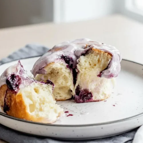 Baked blueberry cinnamon rolls topped with thick cream cheese frosting and rich purple berry swirls.