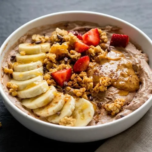 A thick, velvety chocolate peanut butter high protein yogurt bowl topped with fresh berries, banana slices, and crunchy granola.