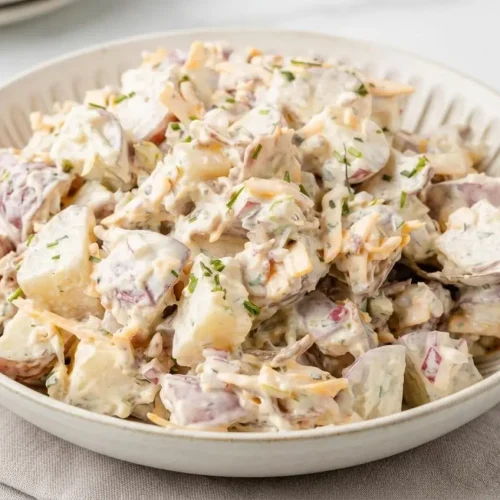 Creamy steakhouse potato salad topped with crispy bacon, shredded cheddar, and fresh chives in a serving bowl.