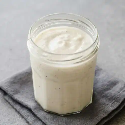 Creamy, glossy white pizza sauce with garlic and parmesan in a bowl, showing a silky, spreadable texture.