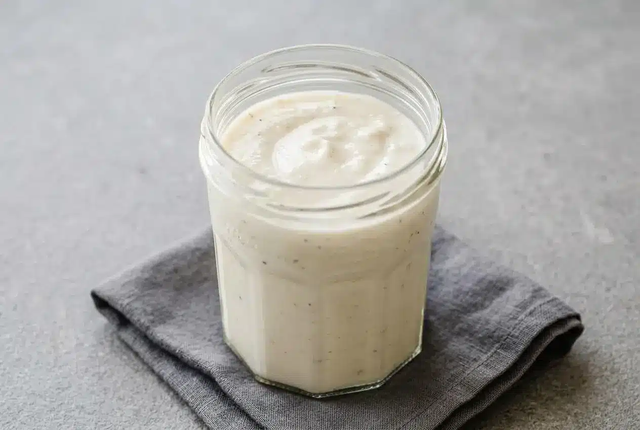 Creamy, glossy white pizza sauce with garlic and parmesan in a bowl, showing a silky, spreadable texture.