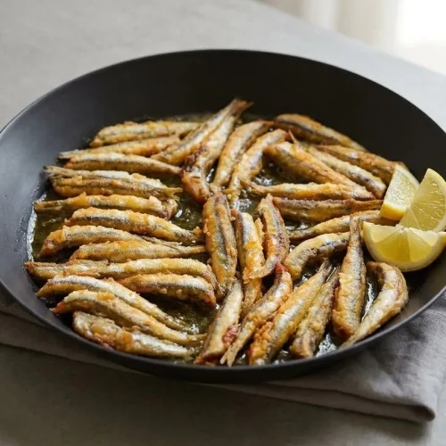 A platter of golden crispy fried anchovies served hot with fresh lemon wedges.