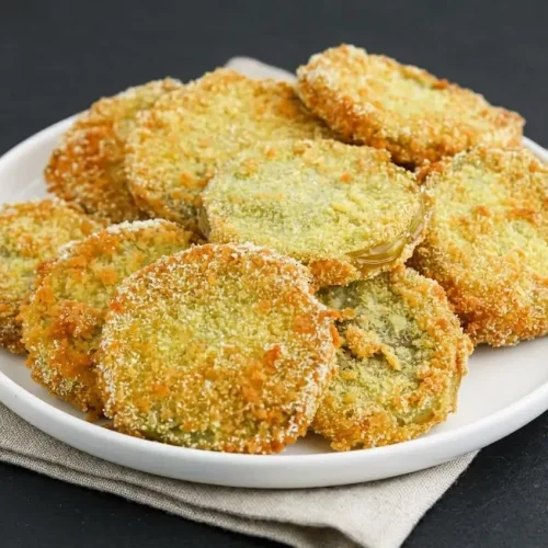 Crispy fried green tomatoes with a golden cornmeal panko crust stacked on a serving plate.