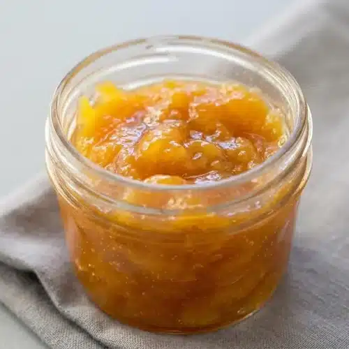 Glossy golden peach jam with a soft spreadable texture in a glass jar.