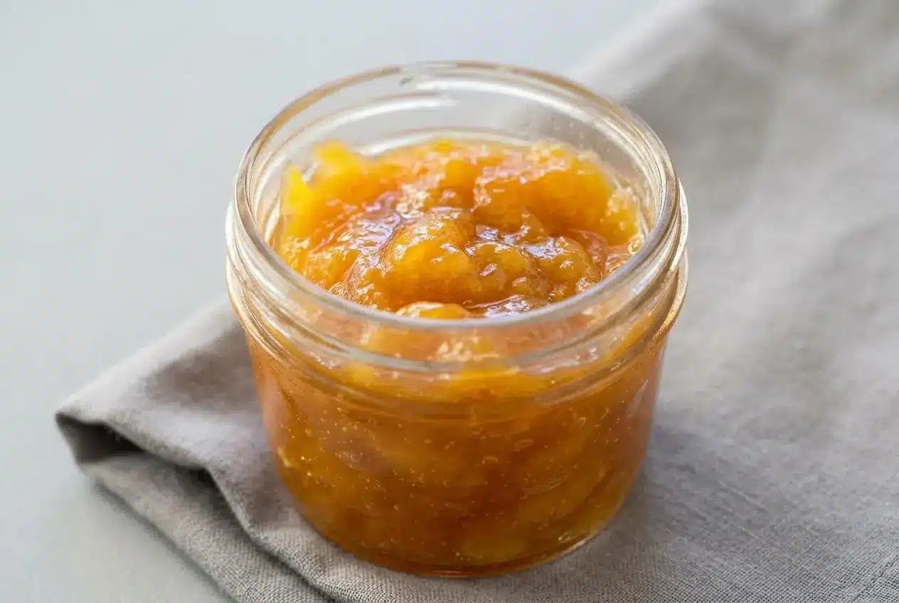 Glossy golden peach jam with a soft spreadable texture in a glass jar.