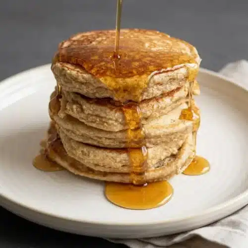 A fluffy stack of golden cottage cheese banana oatmeal protein pancakes topped with sliced banana.