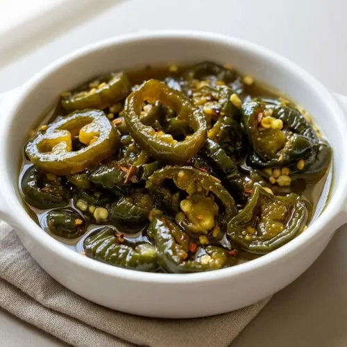 Glossy cowboy candy recipe with sliced green jalapeño peppers coated in a thick, shiny sweet vinegar syrup.