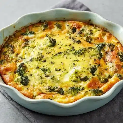 Baked crustless quiche with a golden top and green broccoli florets in a white ceramic dish.