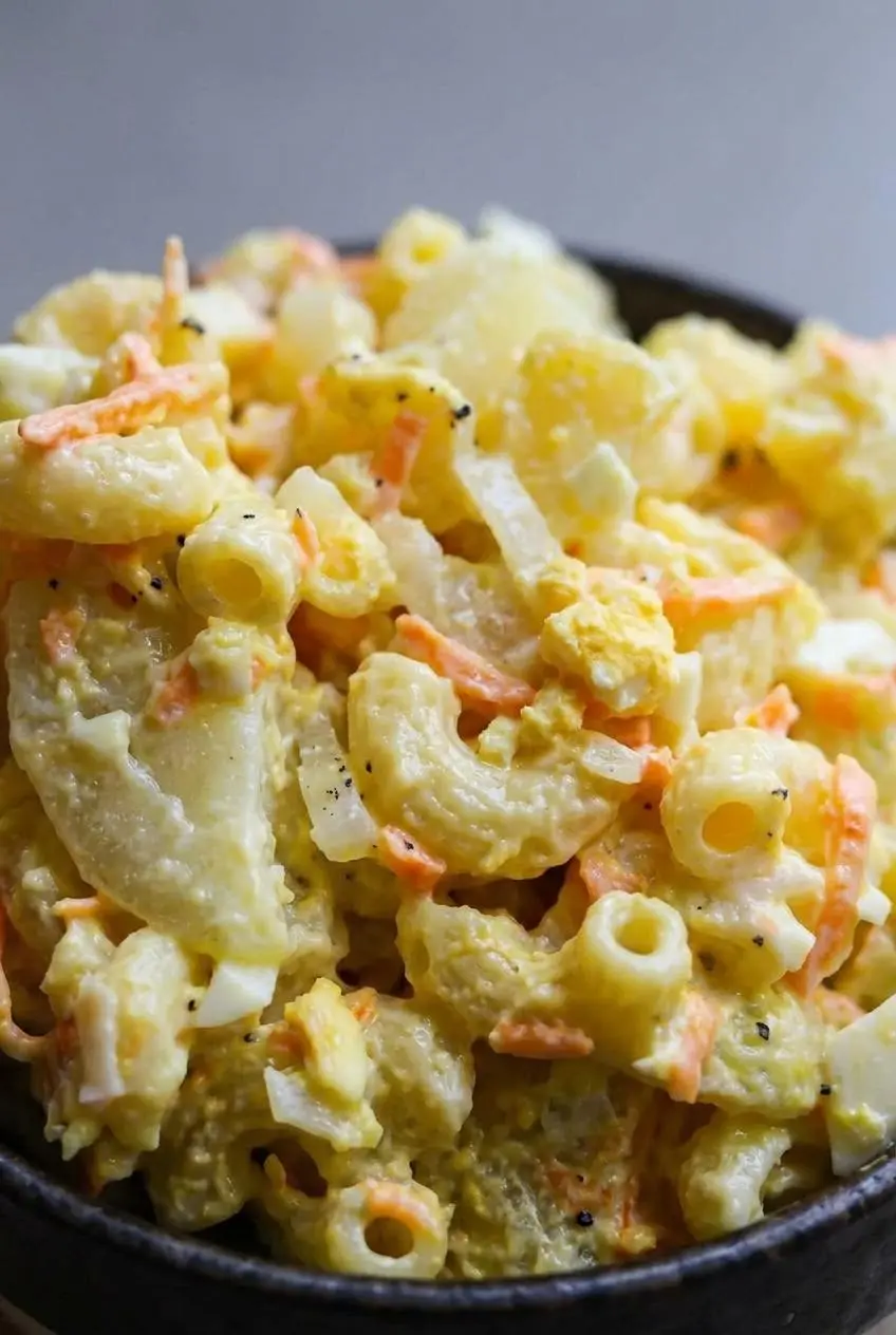 Macro close-up of Hawaiian macaroni salad showing glossy mayonnaise coating, tender pasta curves, and egg crumbs.