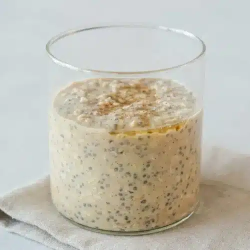A glass jar of high protein overnight oats showing a thick, creamy texture with plump rolled oats and hydrated chia seeds.