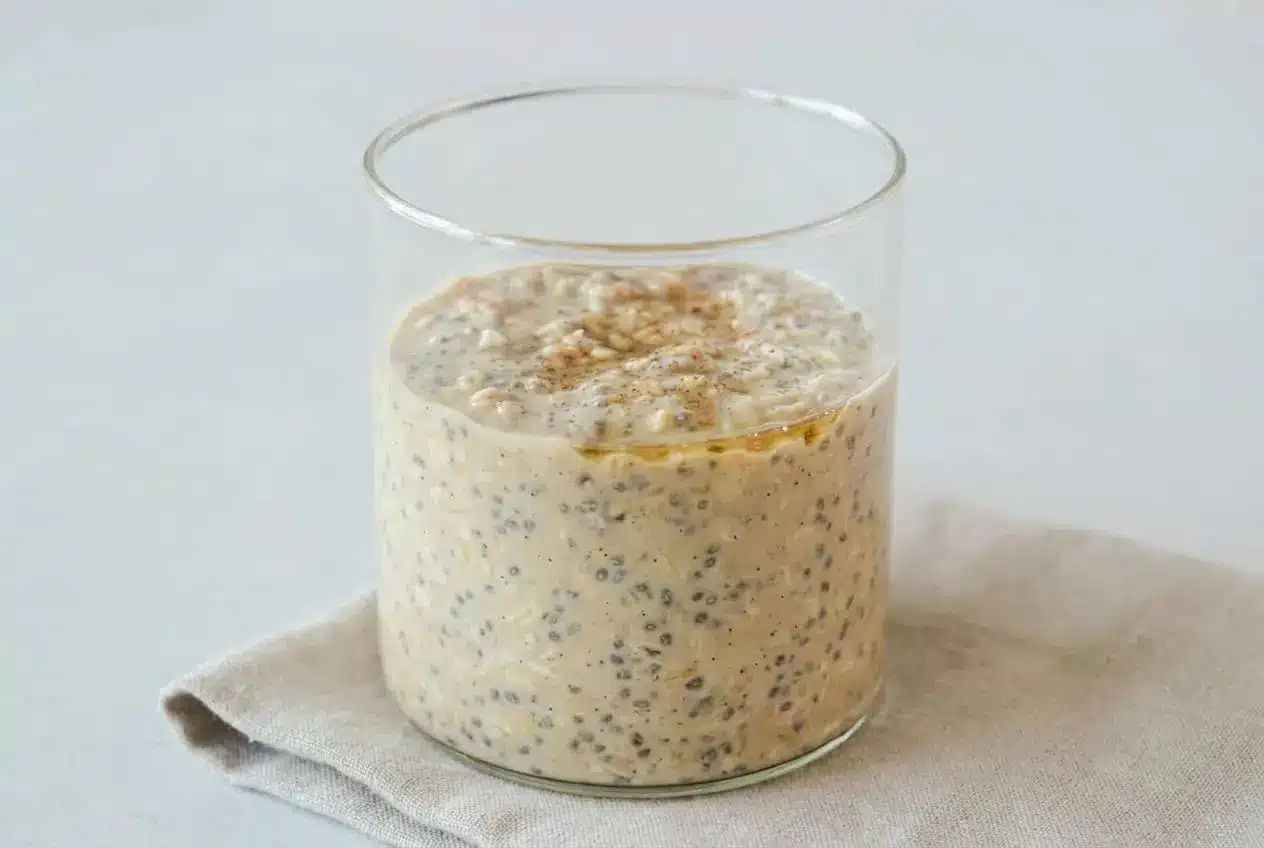A glass jar of high protein overnight oats showing a thick, creamy texture with plump rolled oats and hydrated chia seeds.