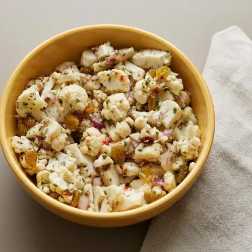 Marinated Cauliflower Salad with crisp raw florets, golden raisins, and herb garlic vinaigrette in a bowl.