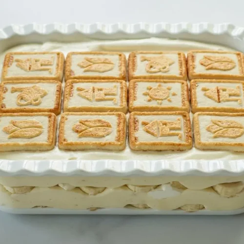 Not Yo Mama's Banana Pudding in a glass dish topped with rows of golden Chessmen cookies.