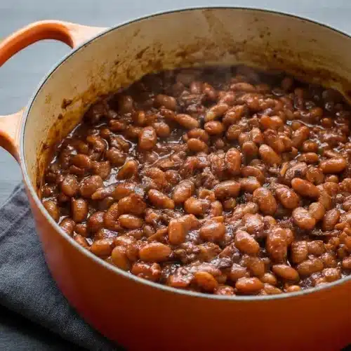 Old fashioned baked beans in a Dutch oven topped with crispy bacon and a thick molasses glaze.