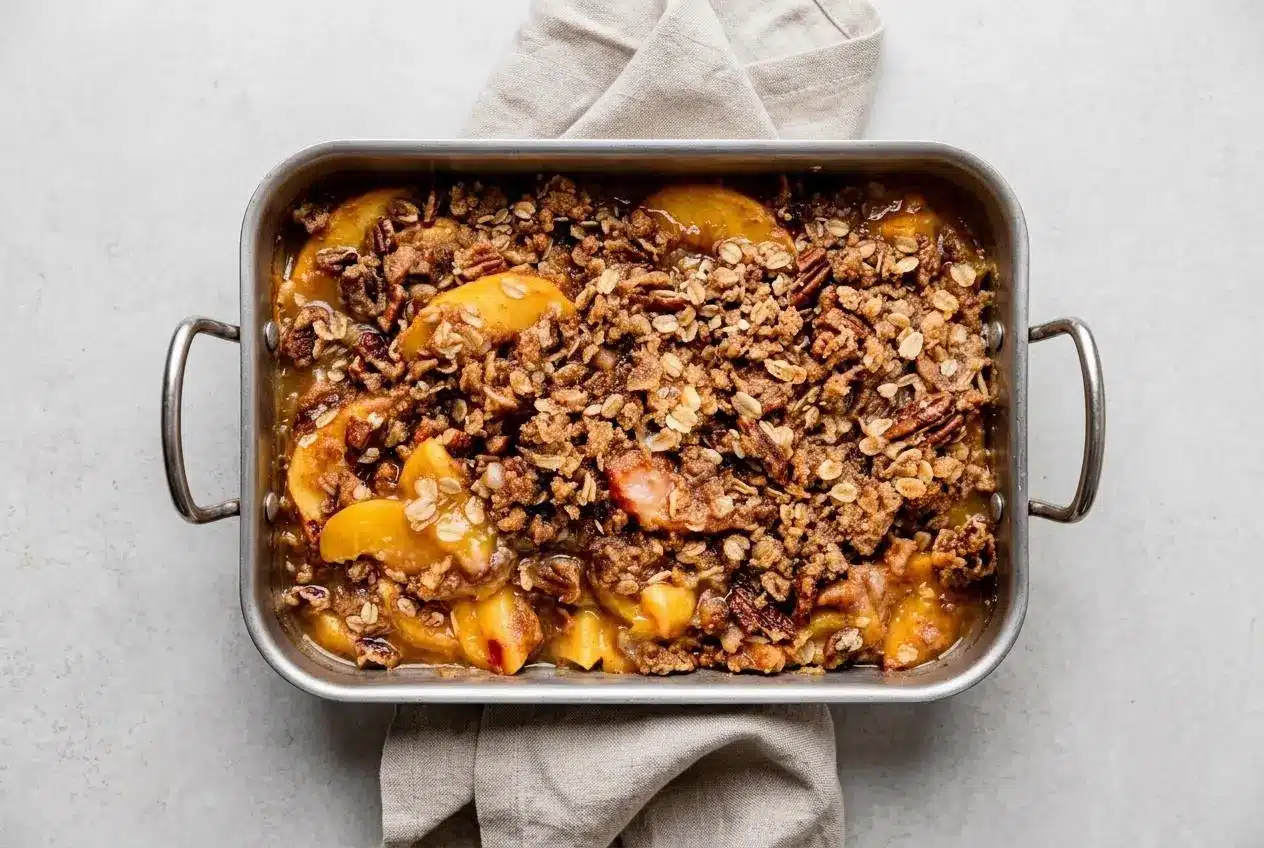 Baked peach crisp recipe with a golden brown oat pecan topping in a deep dish ceramic baking pan.