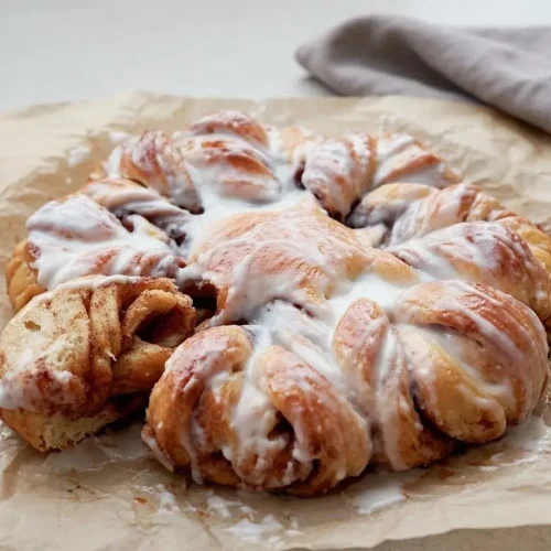 Golden-brown Sourdough Cinnamon Star bread with a glossy glaze on a light cream dish.