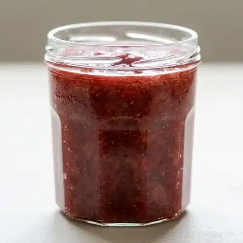 A small glass jar filled with glossy strawberry rhubarb chia jam showing visible fruit pieces and tiny chia seeds.