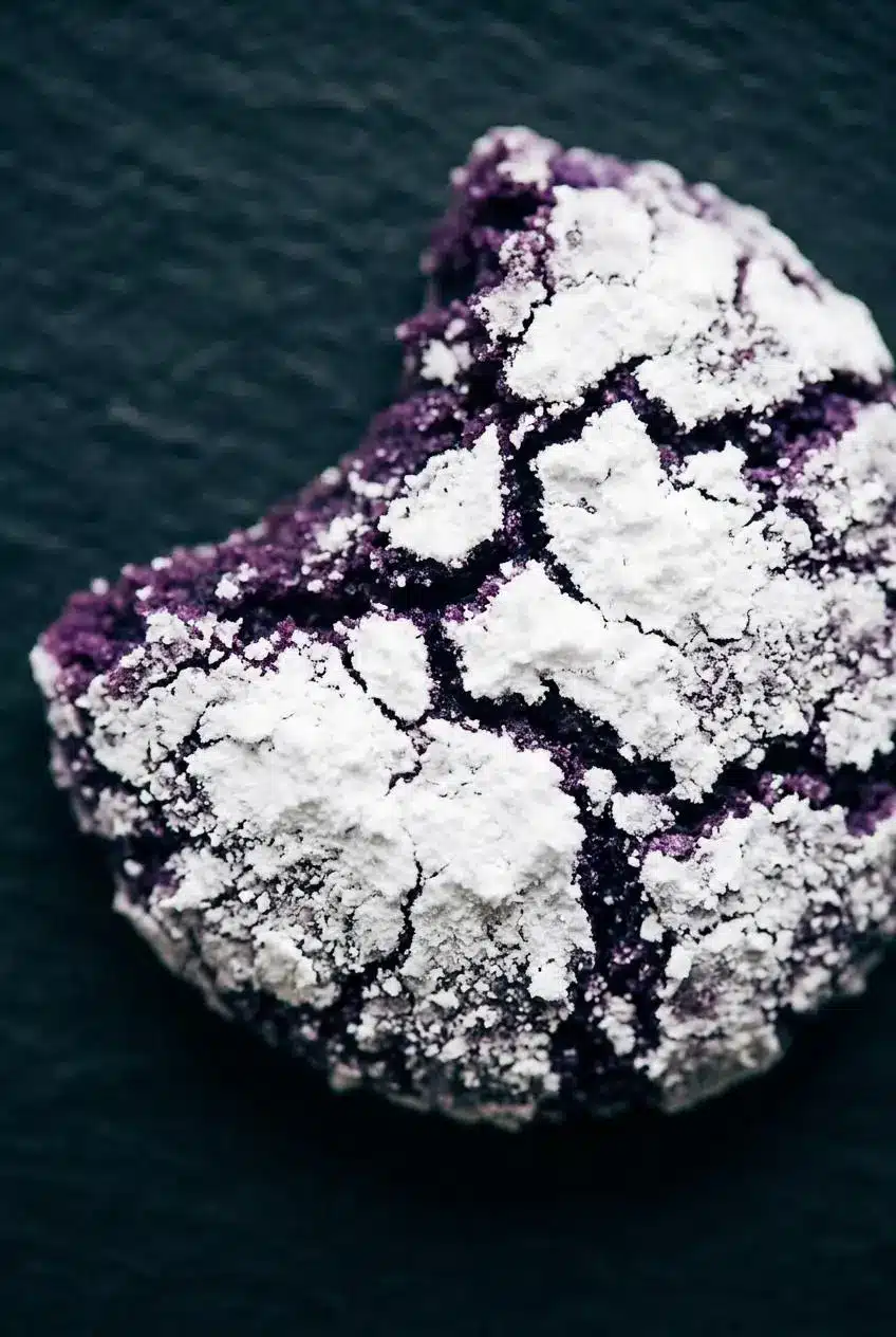 An ultra close up shot of a baked ube crinkle cookie showing deep cracks and vibrant purple interior.