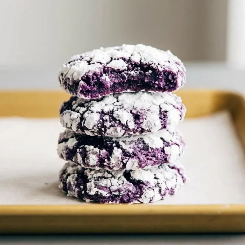 Baked ube crinkle cookies with a vibrant purple center and a snowy white confectioners sugar coating.