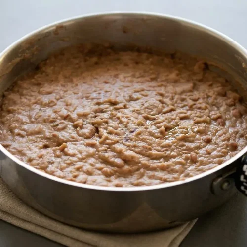 Creamy refried beans recipe showing a glossy finish and rich texture served hot in a cast iron skillet.