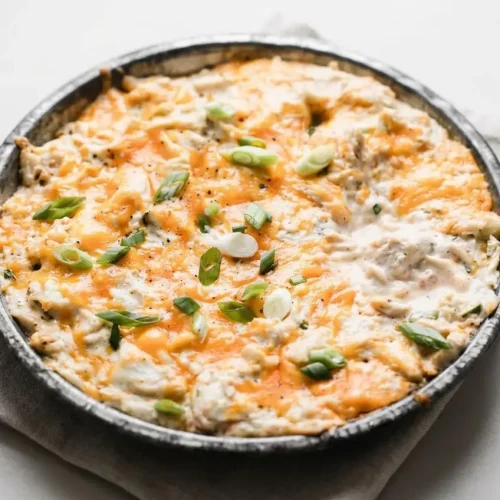 Baked crab dip recipe in a round dish with a golden bubbly cheddar crust and fresh green onions.