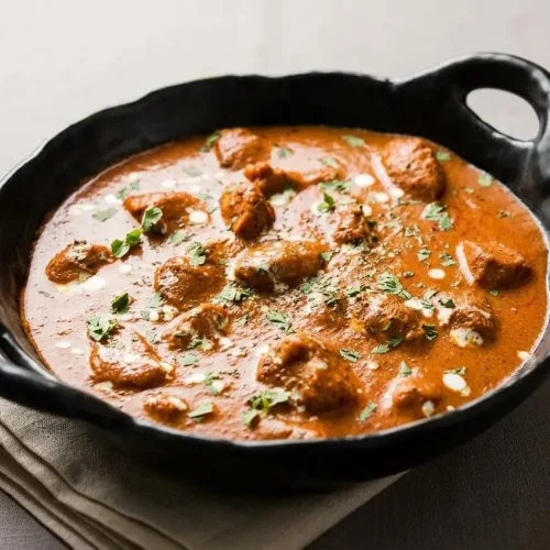 Rich butter chicken recipe in a velvety tomato cashew sauce with charred chicken and a glossy cream swirl.
