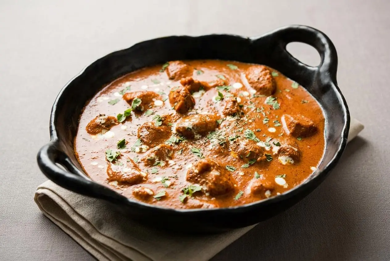 Rich butter chicken recipe in a velvety tomato cashew sauce with charred chicken and a glossy cream swirl.