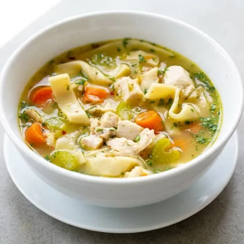 Chicken noodle soup recipe served in a bowl with shredded chicken, egg noodles, carrots, and savory golden broth.