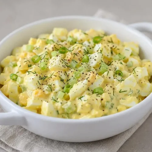Creamy egg salad recipe featuring tender chopped hard-boiled eggs, fresh dill, and crisp celery in a bowl.