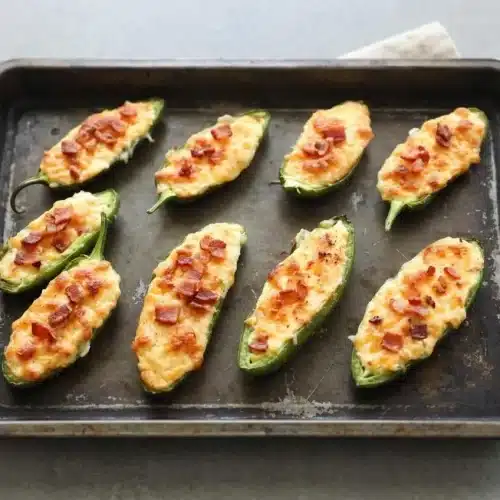 Baked cream cheese jalapeno poppers with blistered golden cheddar topping and tender green pepper halves.