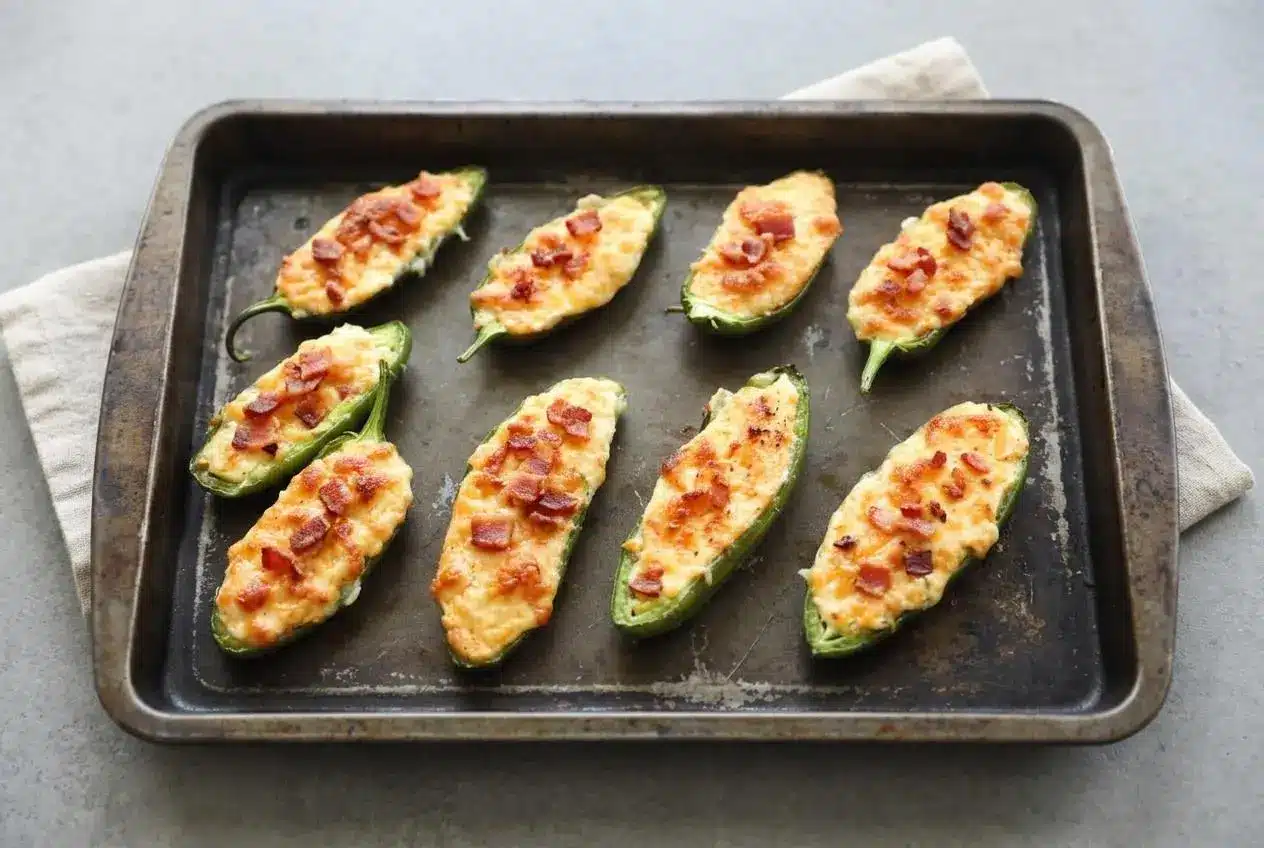 Baked cream cheese jalapeno poppers with blistered golden cheddar topping and tender green pepper halves.
