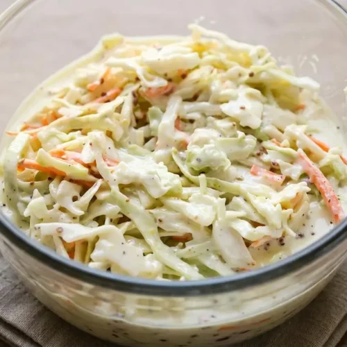 A white bowl of cabbage salad tossed with a creamy, glossy coleslaw dressing recipe and julienned carrots.