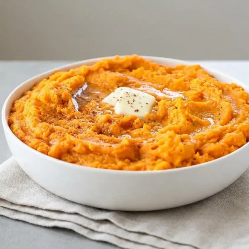Creamy mashed sweet potatoes served in a bowl with melted butter and cracked black pepper.